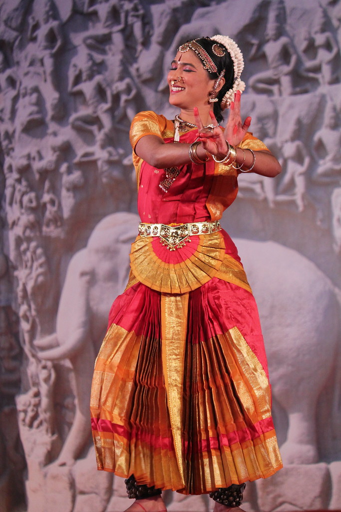 A Bharatanatyam dancer mid-pose on an outdoor stage